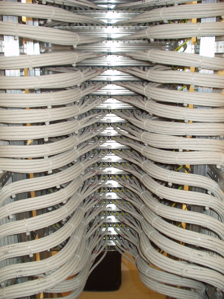 The rear of a tall stack of patch panels where dozens of grey cables are dressed in perfectly parallel horizontal bundles, secured with cable ties, converging symmetrically toward the centre of each panel.