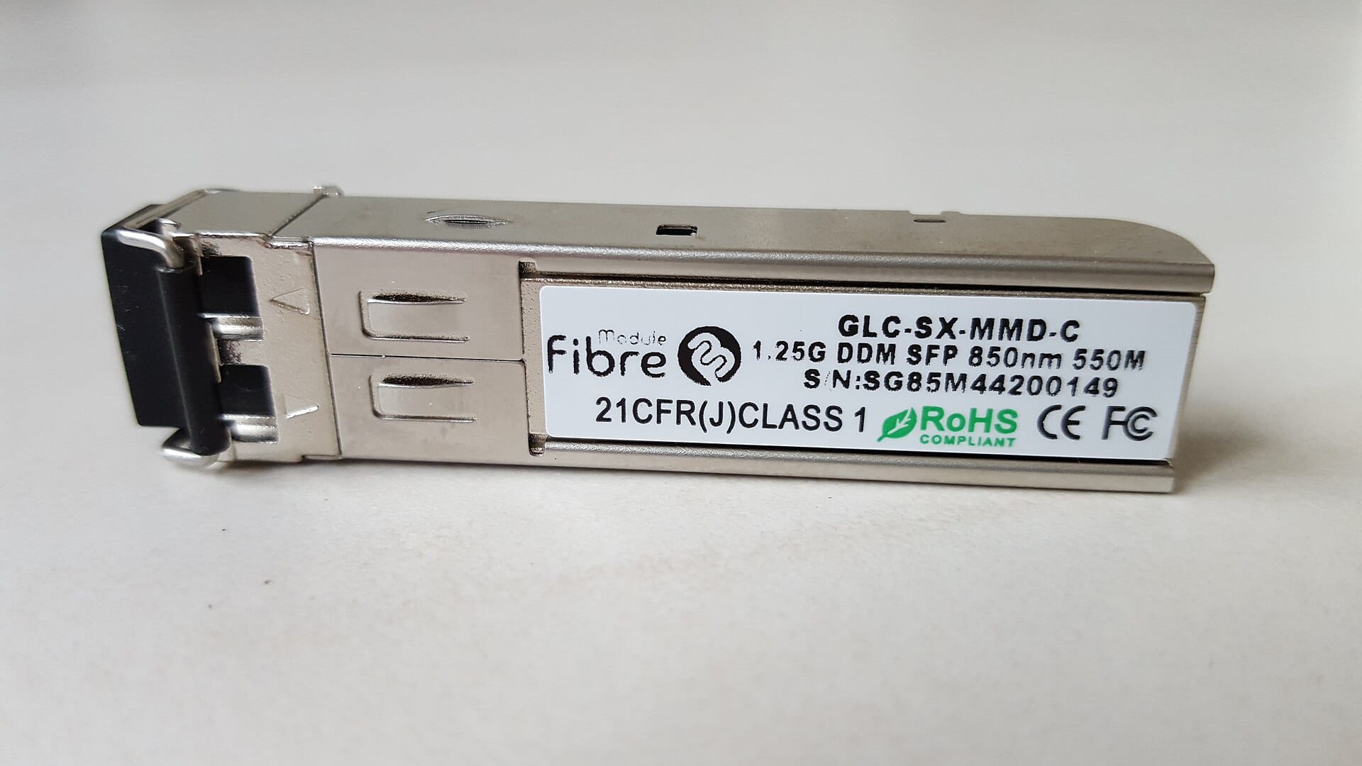 Side view of a small form factor pluggable transceiver module showing its metal casing, the electrical contact edge that inserts into the switch, and the optical port at the front.
