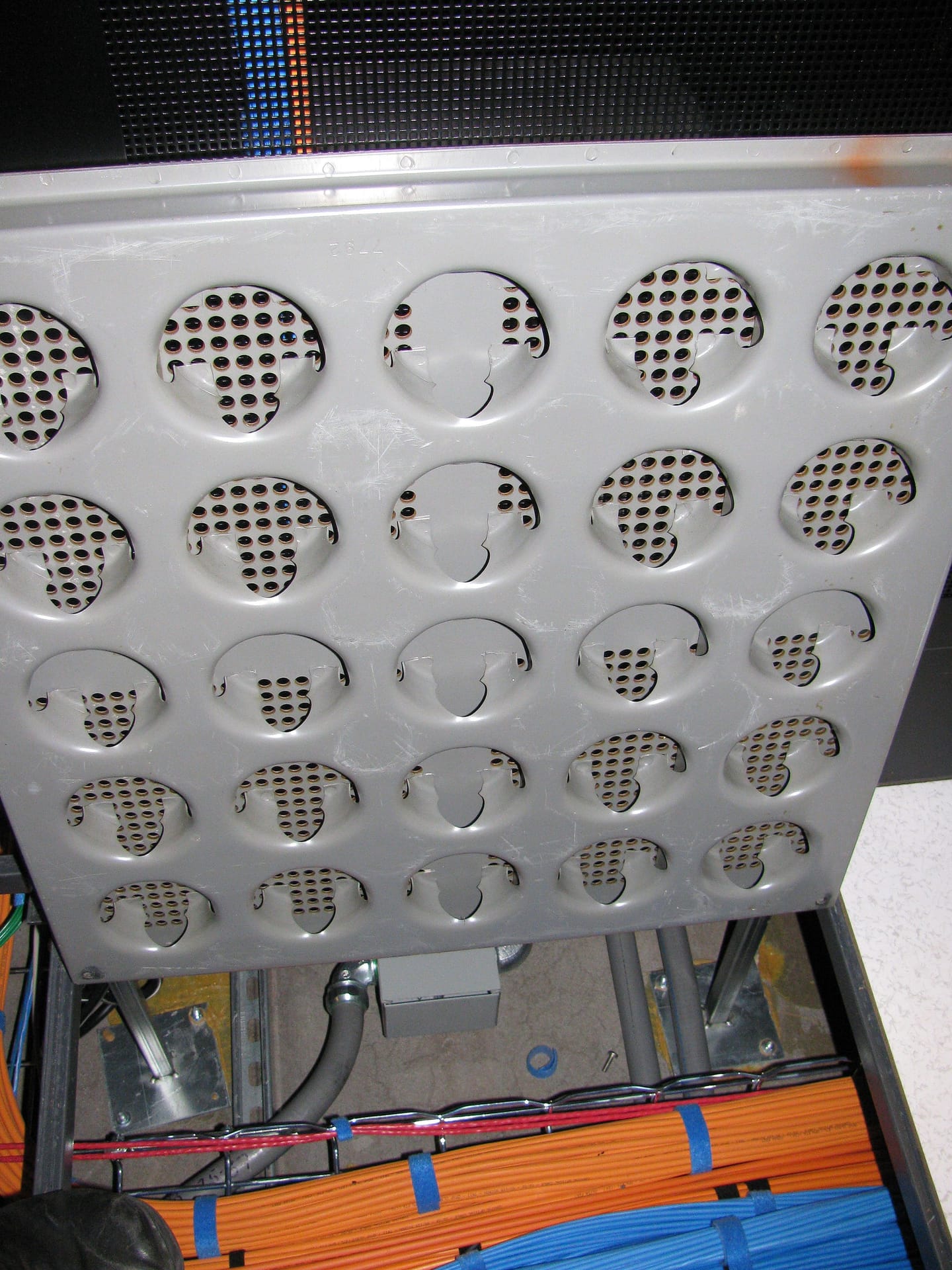 Close up of the underside of a perforated raised floor panel showing the grid of ventilation holes and the panel's structural frame.