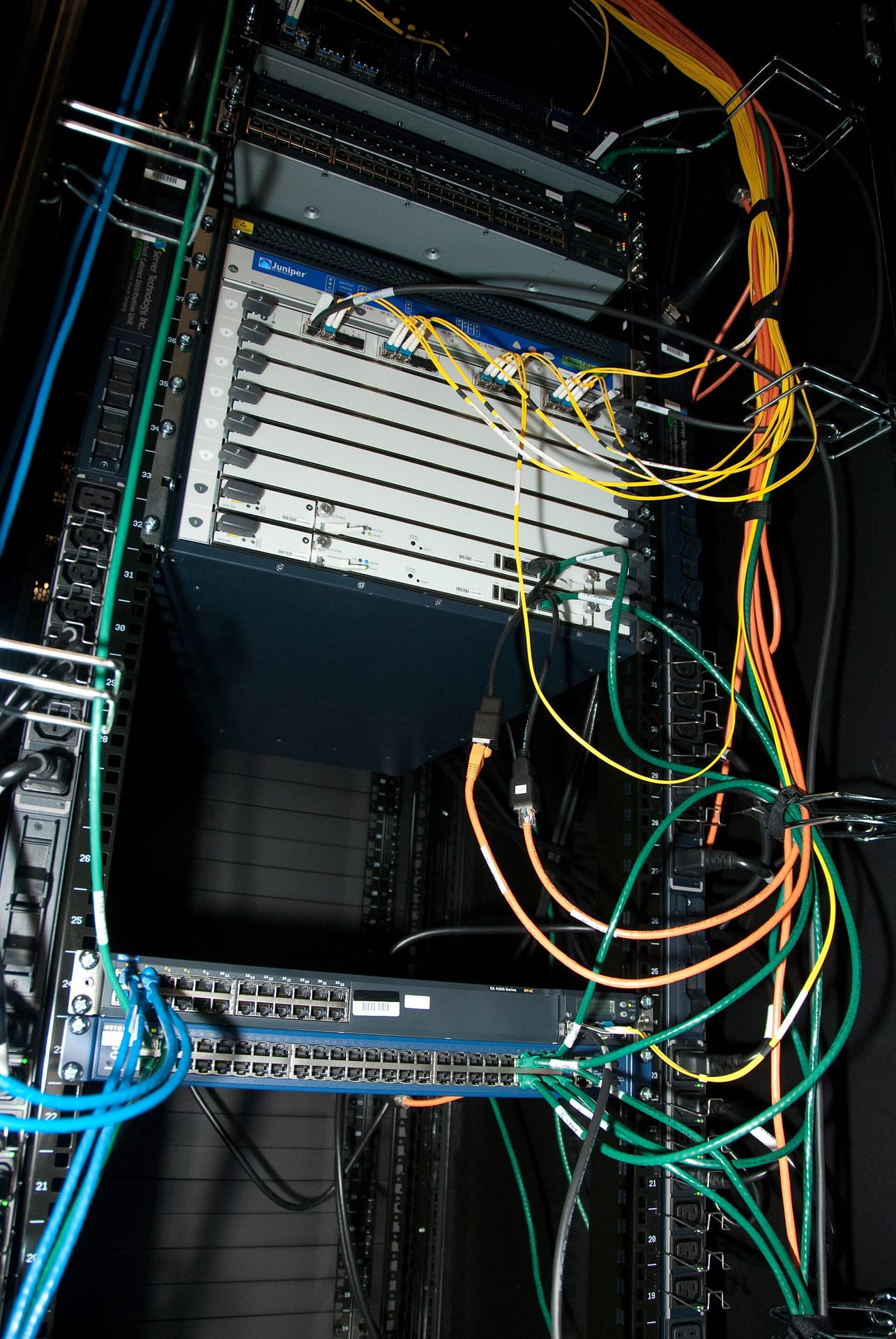 A row of populated server racks in a datacenter with numerous rack mounted servers, network switches, and bundles of cabling running through vertical cable management channels.