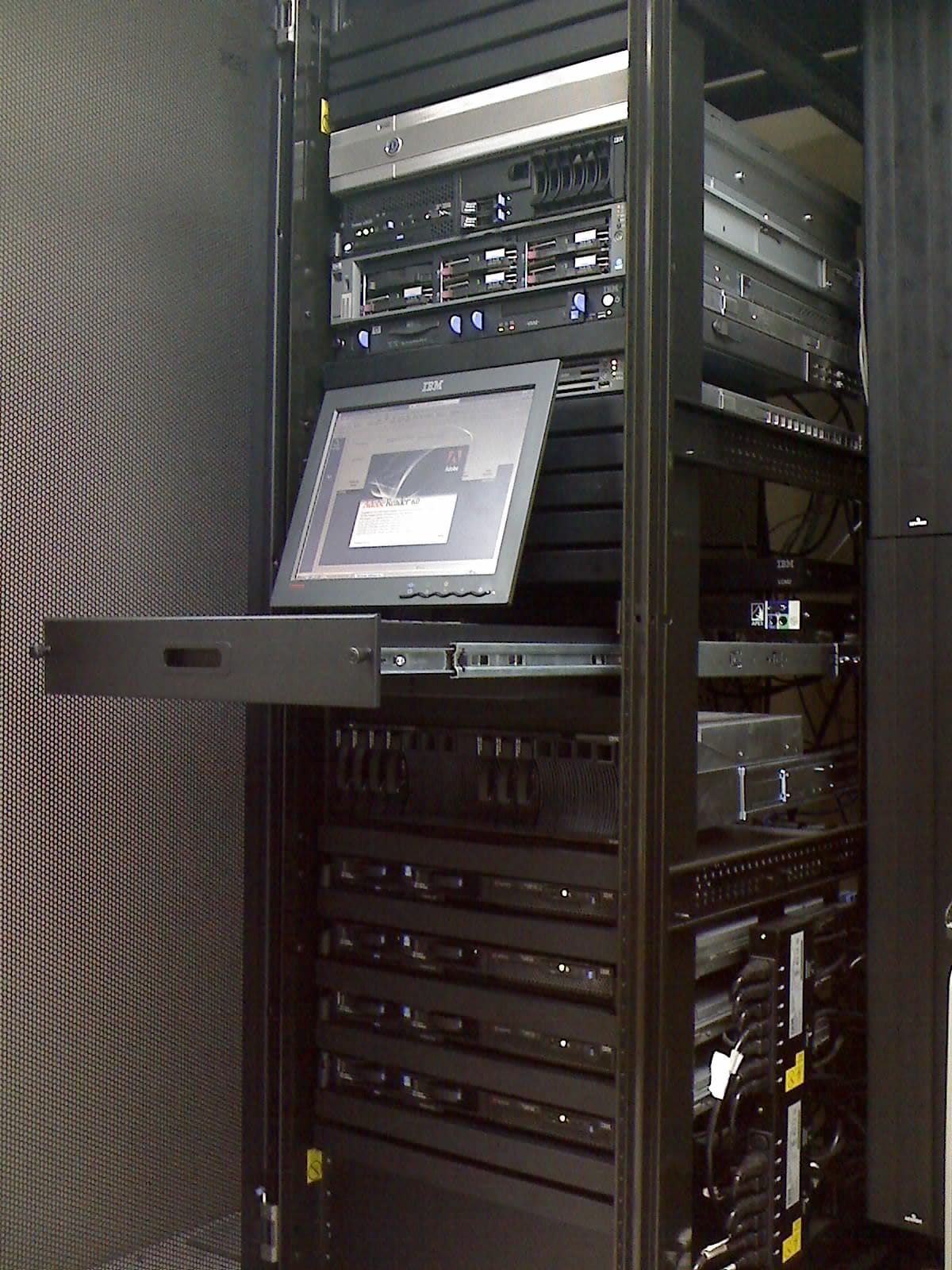 An open server cabinet with several rack mounted servers, a pull out console tray with an LCD screen extended, and cable bundles running down the right hand side.