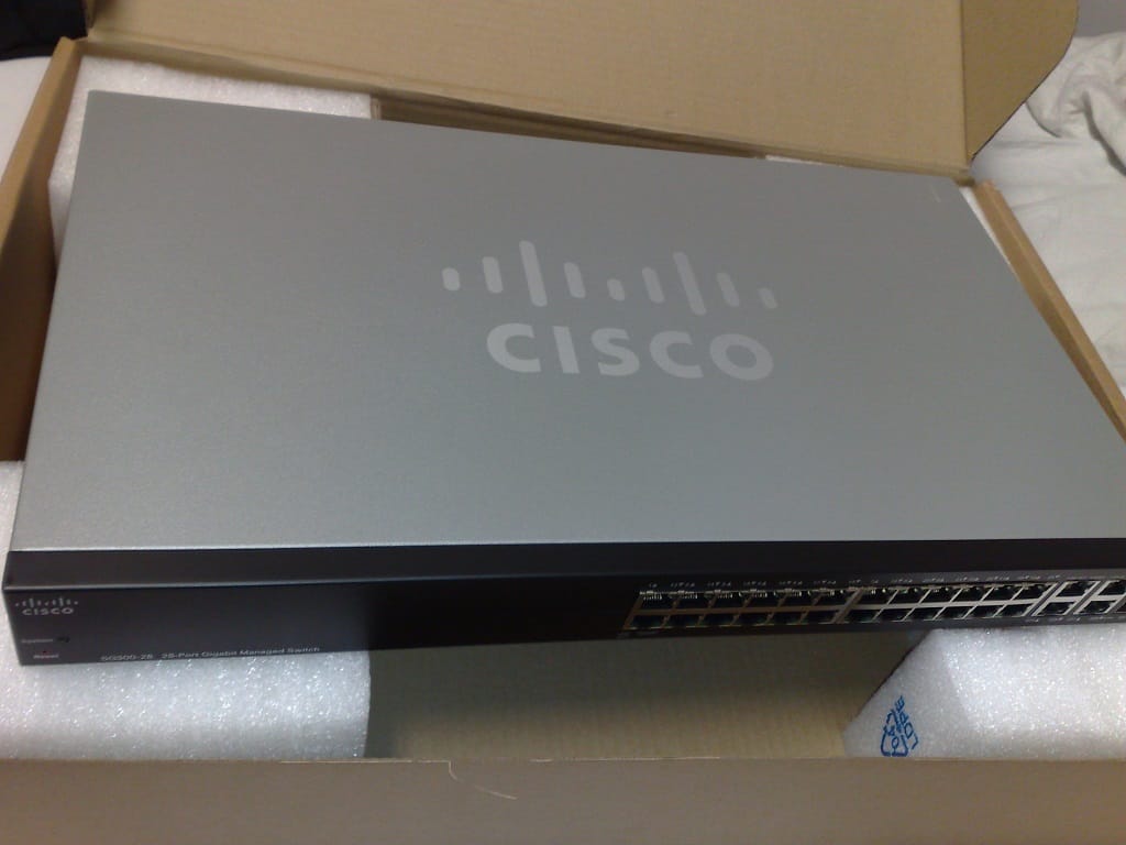Front view of a 28 port rackmount gigabit Ethernet switch with two rows of RJ45 ports, status LEDs above each port, two SFP cages on the right, and rack mounting ears on each side.